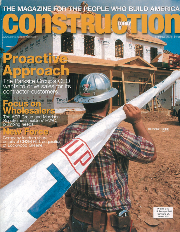 Worker in hard hat carries white pipe at building site.